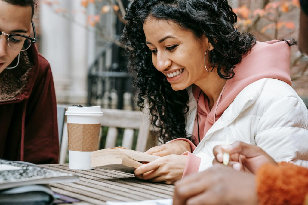 Two university students sit opposite each other at a wooden table in a coffee shop, engaged in a serious conversation.
