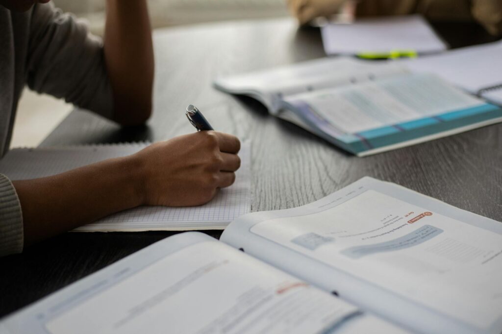 A focused student with a pen in hand diligently writes notes in a notebook during a university lecture.