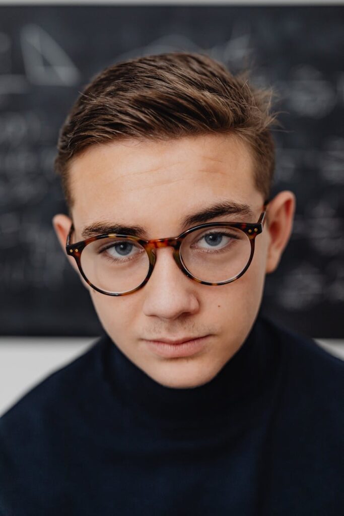 A young male student with glasses looking intently at a professor during a university lecture hall.