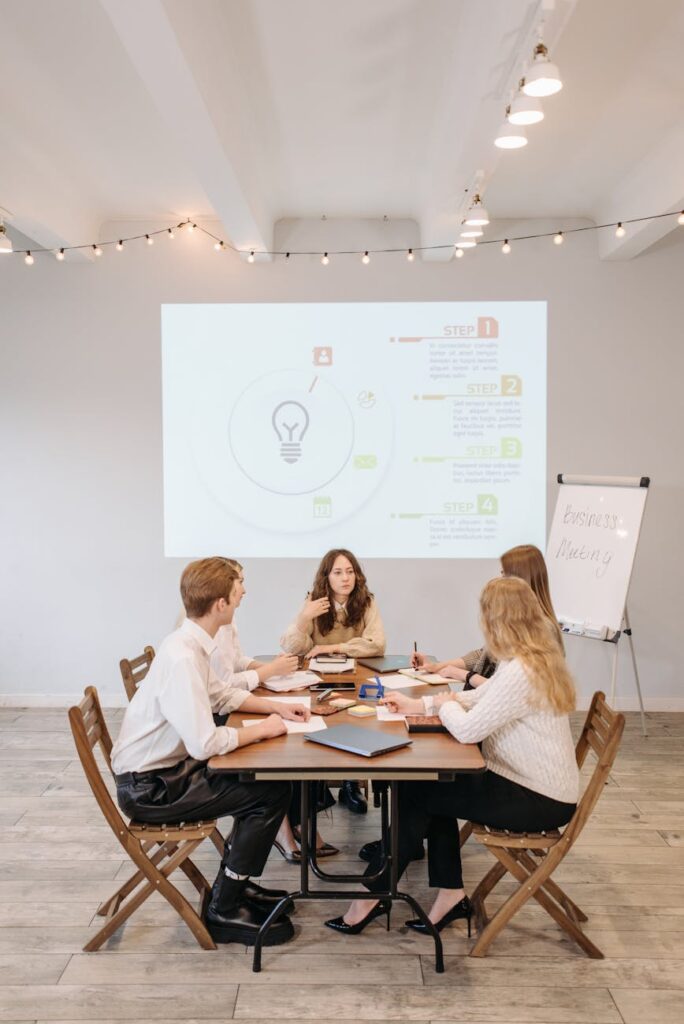 A diverse team of business professionals brainstorming around a whiteboard covered in complex flowcharts and strategic plans for new technology.