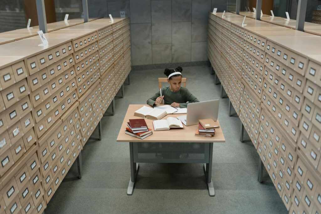 A close-up shot of a young female student with glasses concentrating on her work on a laptop in a bright, modern library.