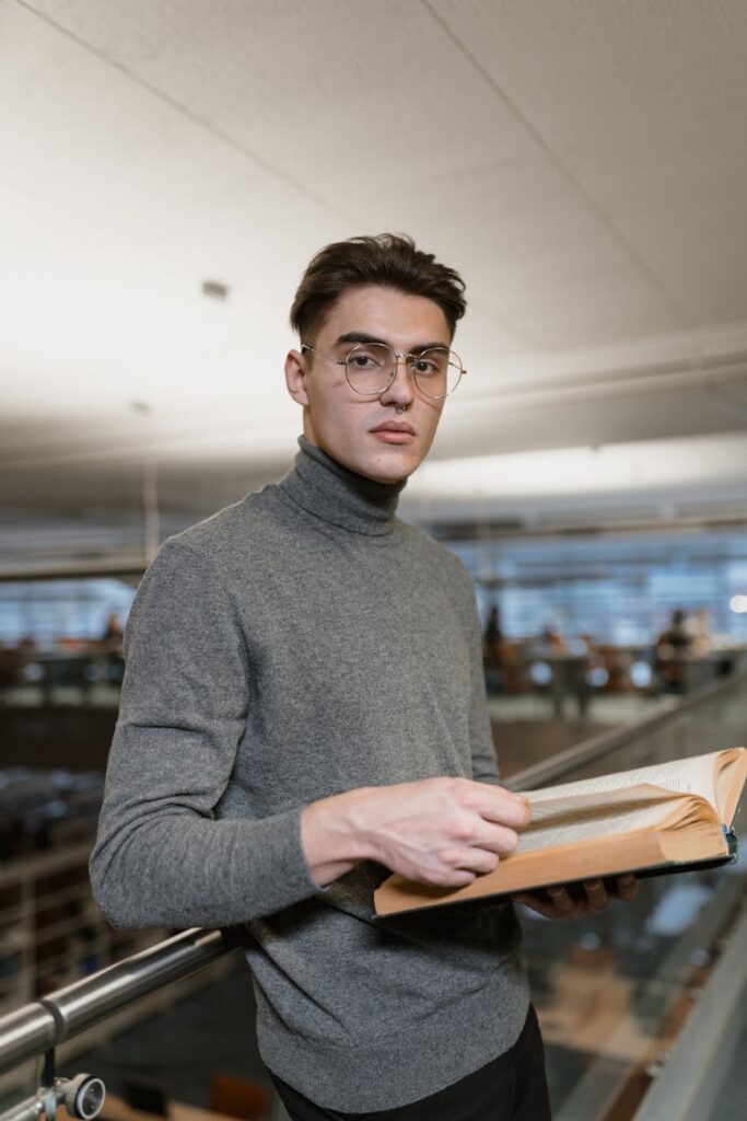 A young student wearing headphones, focused on their laptop screen in a quiet university library.