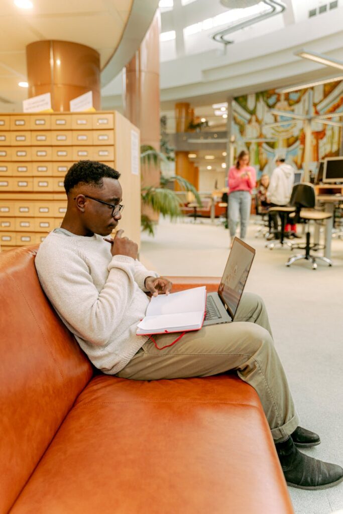 A stressed student sits with their head in their hands, surrounded by stacks of textbooks and a glowing laptop screen.