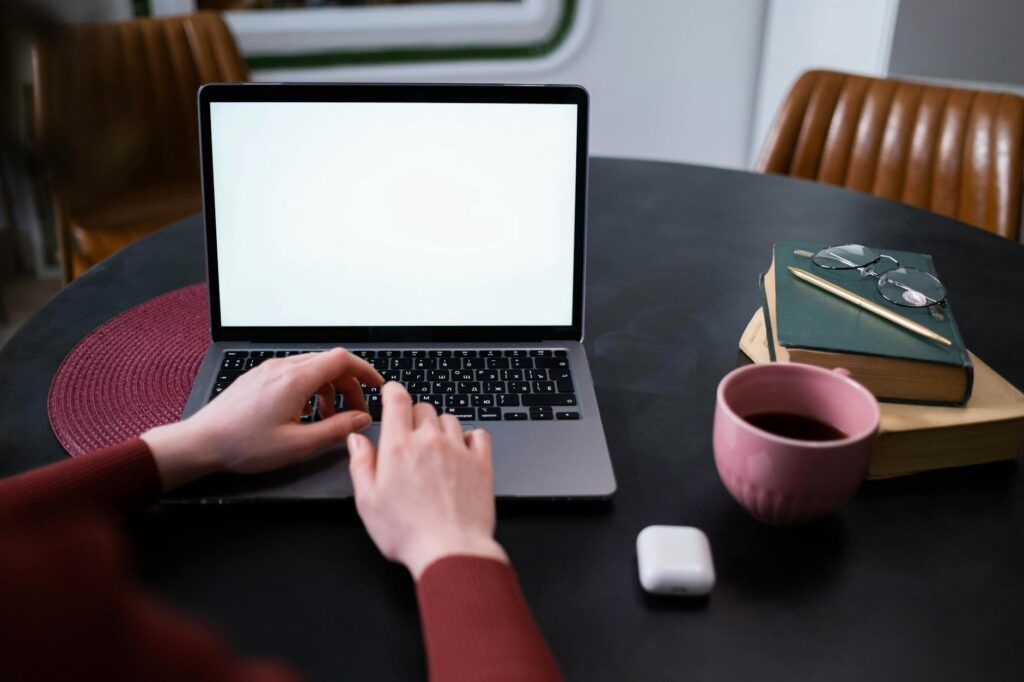 A close-up shot of a student's hands typing quickly on a laptop keyboard with a notebook nearby.
