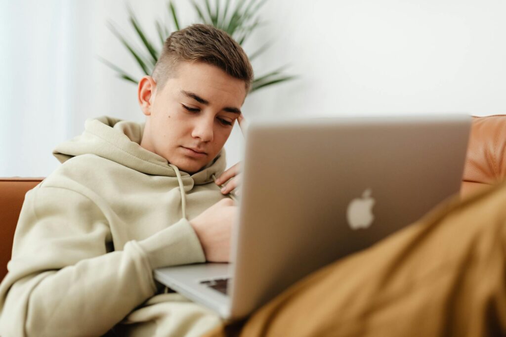 A college student sits on their bed, focused on a laptop screen displaying a banking application.