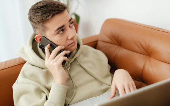 A young student sits alone in a dimly lit dorm room, the glow of their laptop screen illuminating their face.