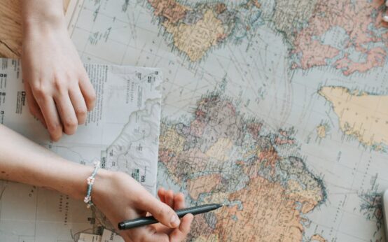 A traveler points to a location on a large, detailed world map, planning their next adventure.
