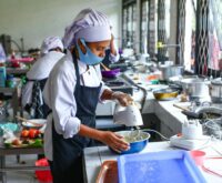 A college student smiles while chopping vegetables in a small but organized dorm kitchen.