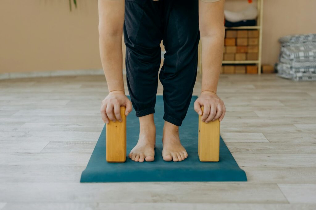 A woman in a yoga pose with her feet in focus, a glass of detox water sits beside her mat.