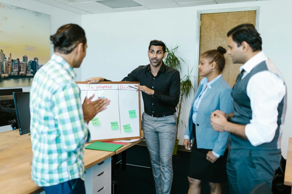 A diverse team of professionals brainstorming business strategy around a whiteboard covered in notes and diagrams.