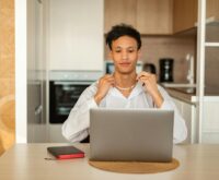 A focused student with headphones on, working on a laptop in a brightly lit coffee shop.