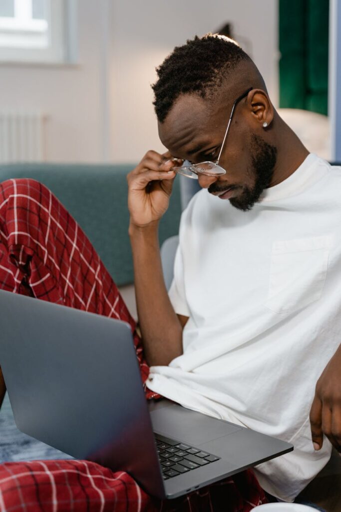 A focused student wearing headphones types on a laptop in a bright, modern library with bookshelves in the background.