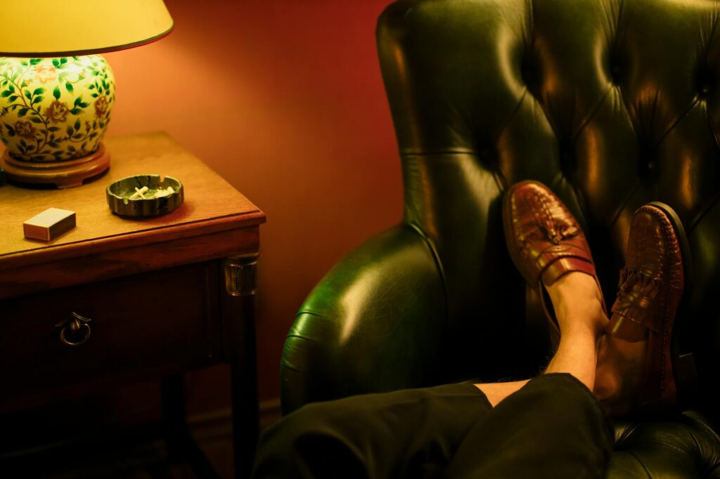 A person wearing comfortable slippers with their feet on a soft rug, a warm drink sits on a wooden end table.