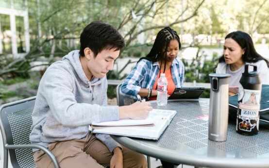 A diverse group of university students working together on laptops in a sunlit, modern library.
