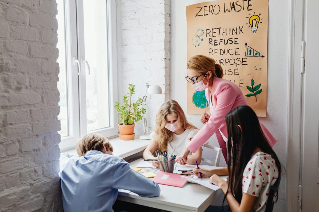 Four students work together on a laptop in a bright, modern classroom setting.