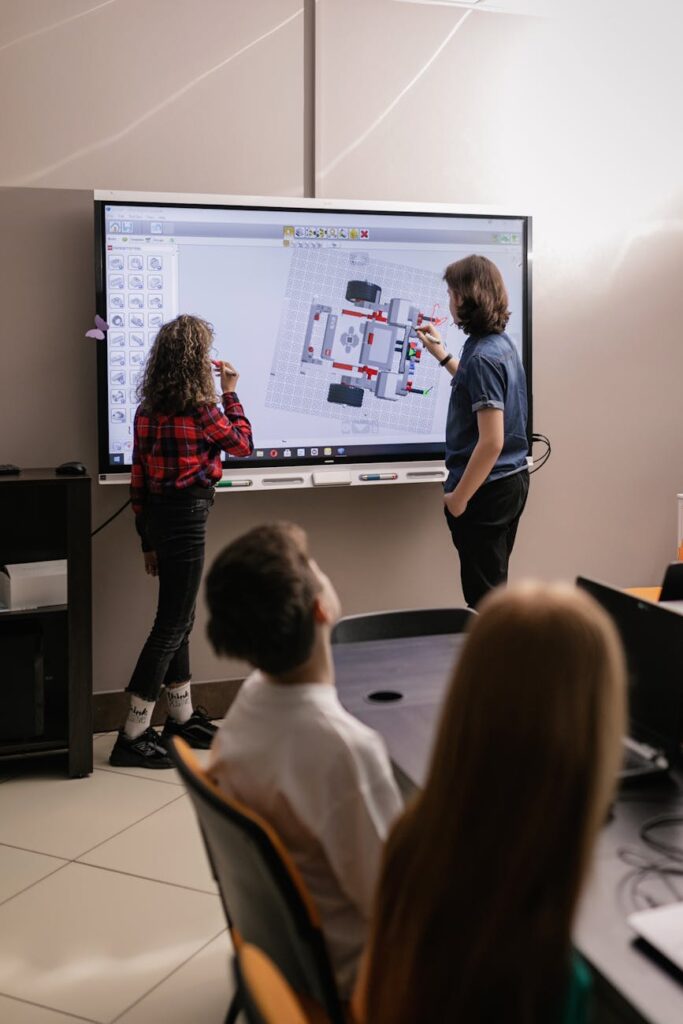 Two students sitting side-by-side, pointing at a tablet screen while working on a school project.