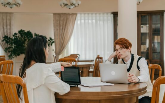 A focused university student with headphones on, studying at a wooden table in a sunlit library.