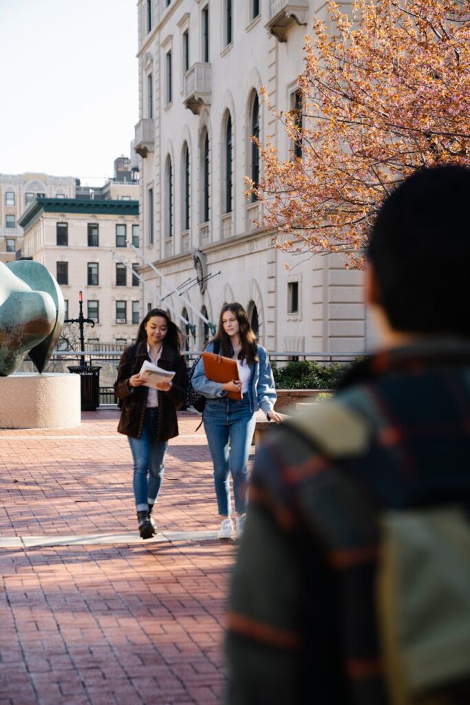 A wide shot of students with backpacks walking between classes on a sunny, modern college campus.