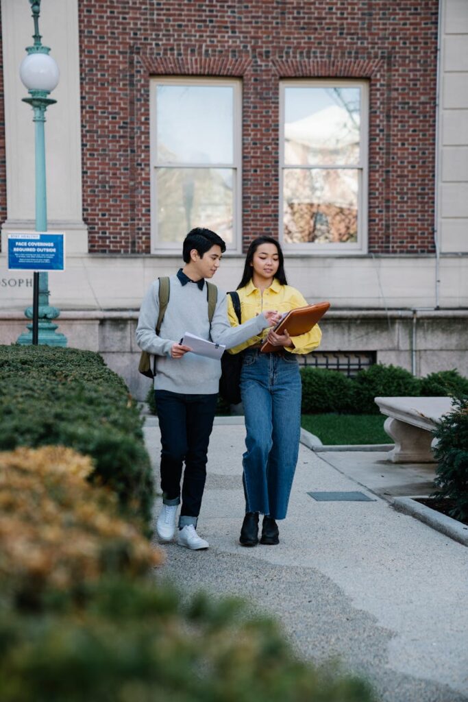 An energetic and diverse group of college students walking and talking together on a sunny campus pathway.