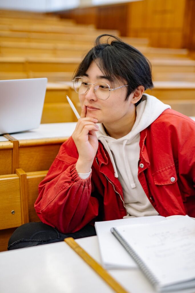 A detailed shot of a student's hands writing notes in a spiral notebook with a pen during a university lecture.