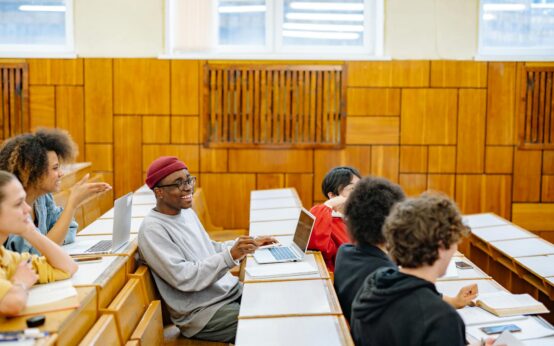A diverse group of high school students gathered around a table, engaged in learning on their digital tablets.