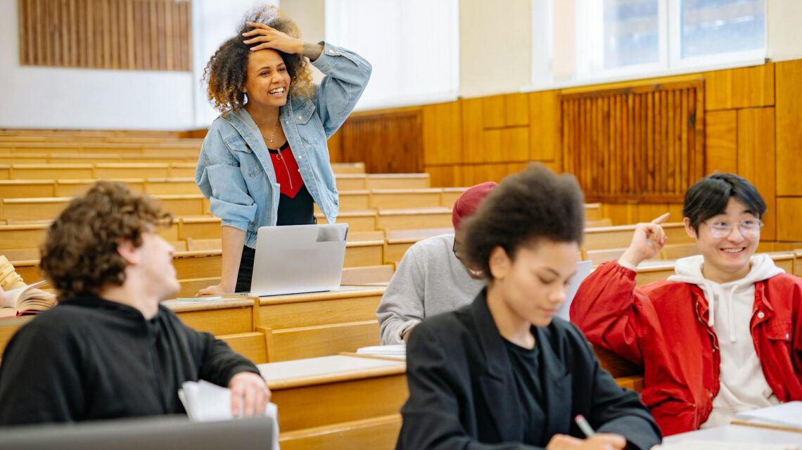 A diverse group of male and female university students working together around a table with laptops and notebooks.