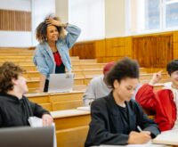 A diverse group of male and female university students working together around a table with laptops and notebooks.