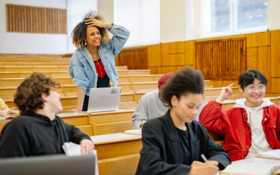 A diverse group of male and female university students working together around a table with laptops and notebooks.