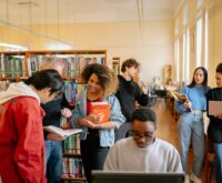 A diverse group of male and female students working together on their laptops at a large table.