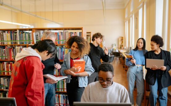 A diverse group of male and female students working together on their laptops at a large table.