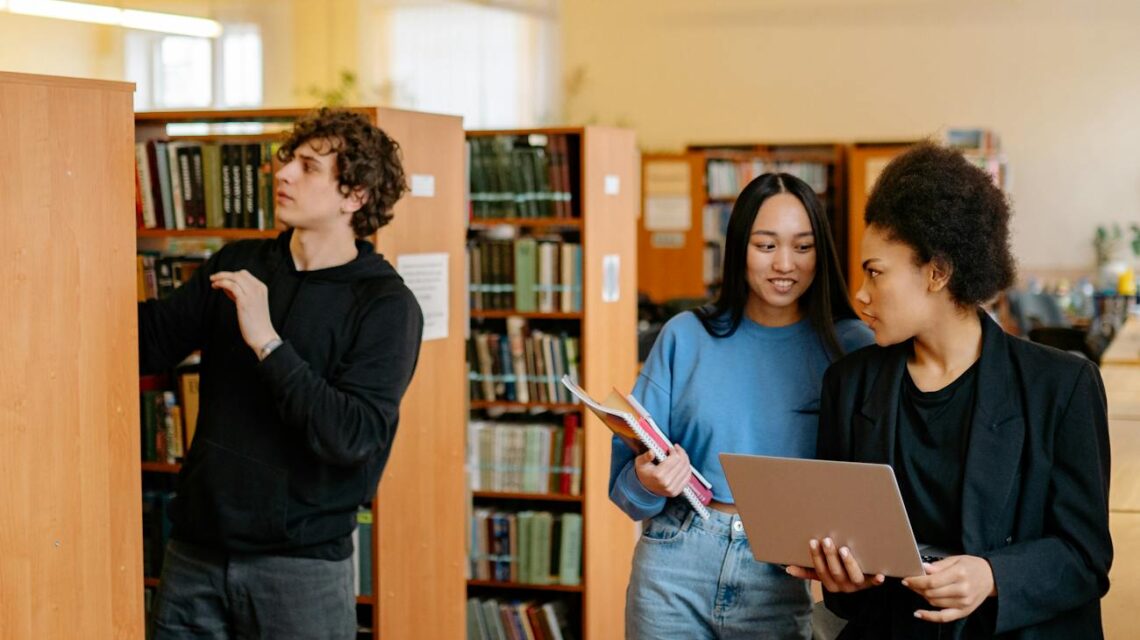 A diverse group of college students sit around a table, working together on a project with a laptop.