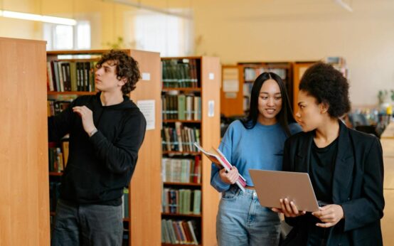 A diverse group of college students sit around a table, working together on a project with a laptop.
