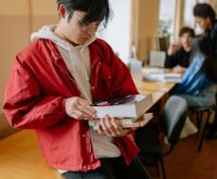 A focused college student with headphones on, studying at a wooden table in a sunlit library.