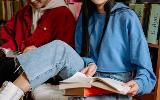 A diverse group of four university students sitting at a table with books and laptops, engaged in a discussion.