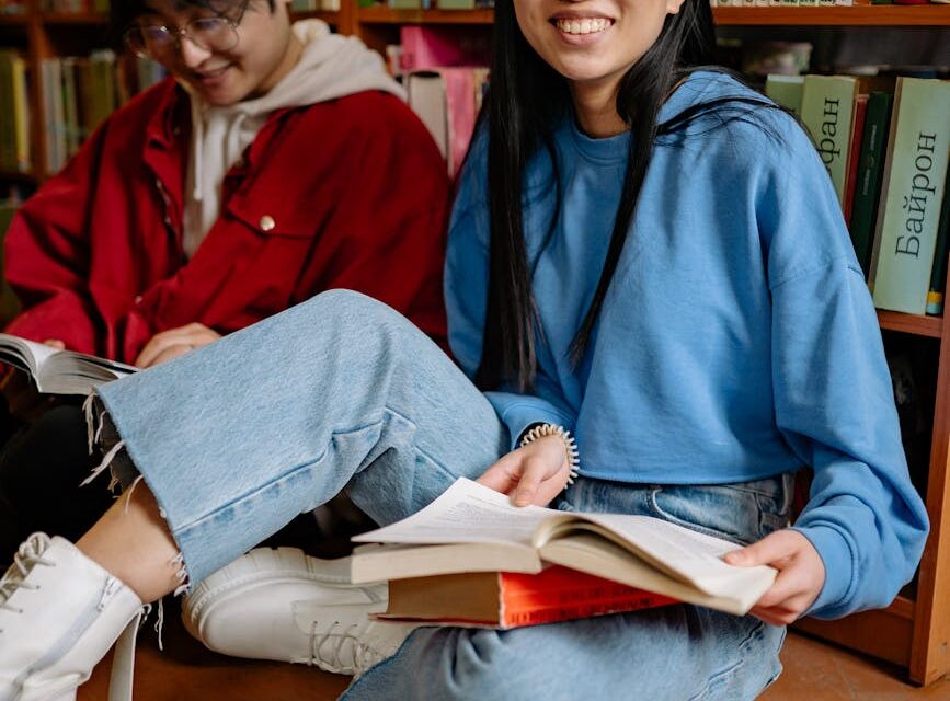 A diverse group of four university students sitting at a table with books and laptops, engaged in a discussion.