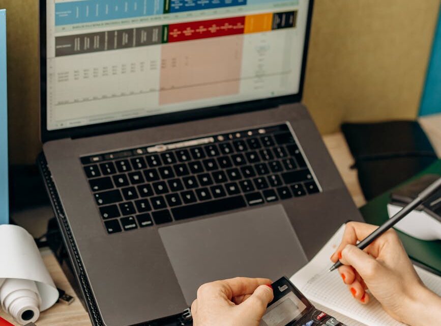 A close-up of a person's hands using a calculator next to a pile of financial reports and a coffee mug.