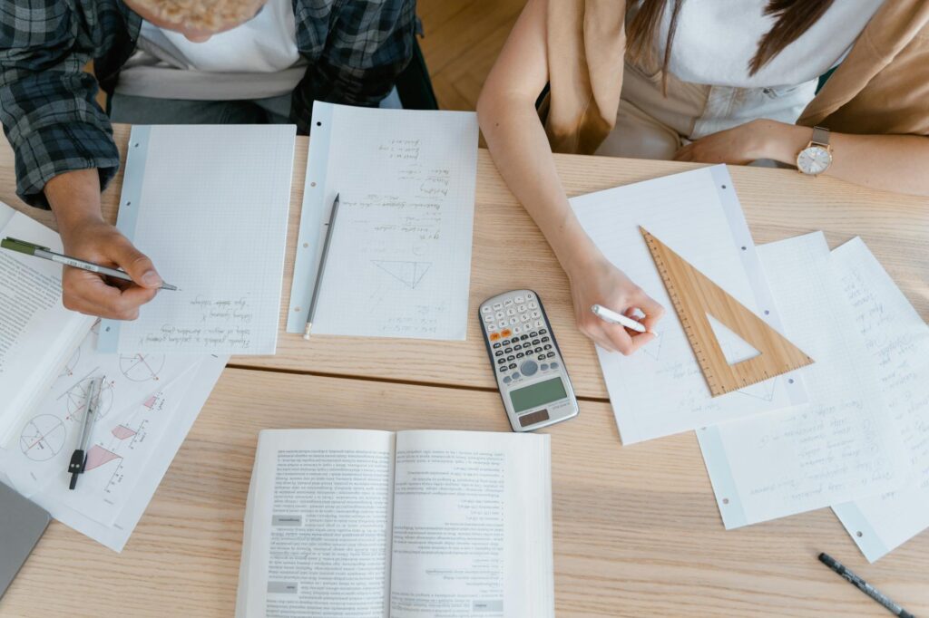 Close-up of a student's hands using a calculator and writing notes in a notebook, planning their finances.