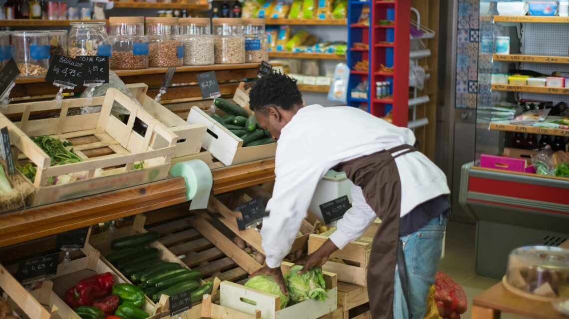 A person with a shopping cart closely examining the nutritional information on the back of a food package.