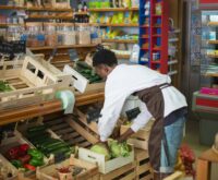 A person with a shopping cart closely examining the nutritional information on the back of a food package.