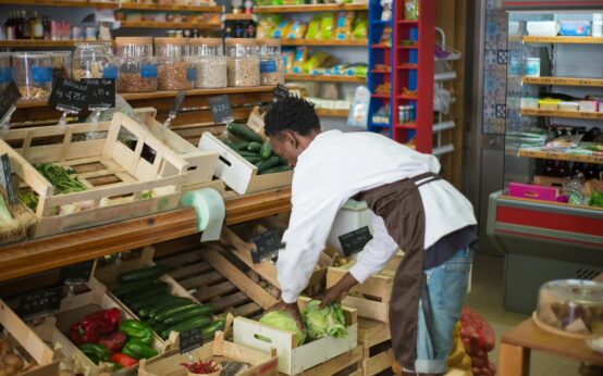 A person with a shopping cart closely examining the nutritional information on the back of a food package.