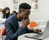 A student carefully highlighting text on a printed document next to an open laptop.
