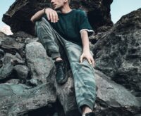 A lone hiker stands on a mountain peak, silhouetted against a vast sky filled with fluffy white clouds.