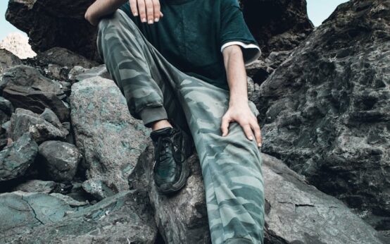 A lone hiker stands on a mountain peak, silhouetted against a vast sky filled with fluffy white clouds.