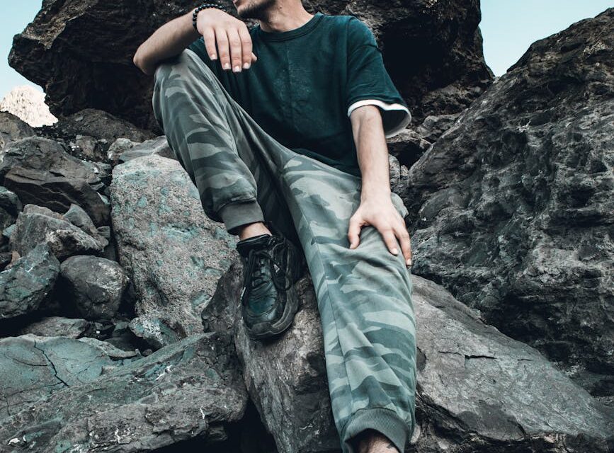 A lone hiker stands on a mountain peak, silhouetted against a vast sky filled with fluffy white clouds.
