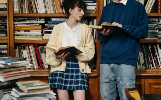 A diverse group of university students focused on their books and laptops in a sunlit library.
