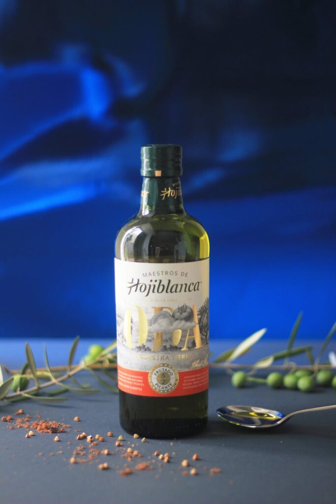 A hand holding a bottle of extra virgin olive oil, pouring it over a cooked fish and vegetable dish, emphasizing healthy fats.